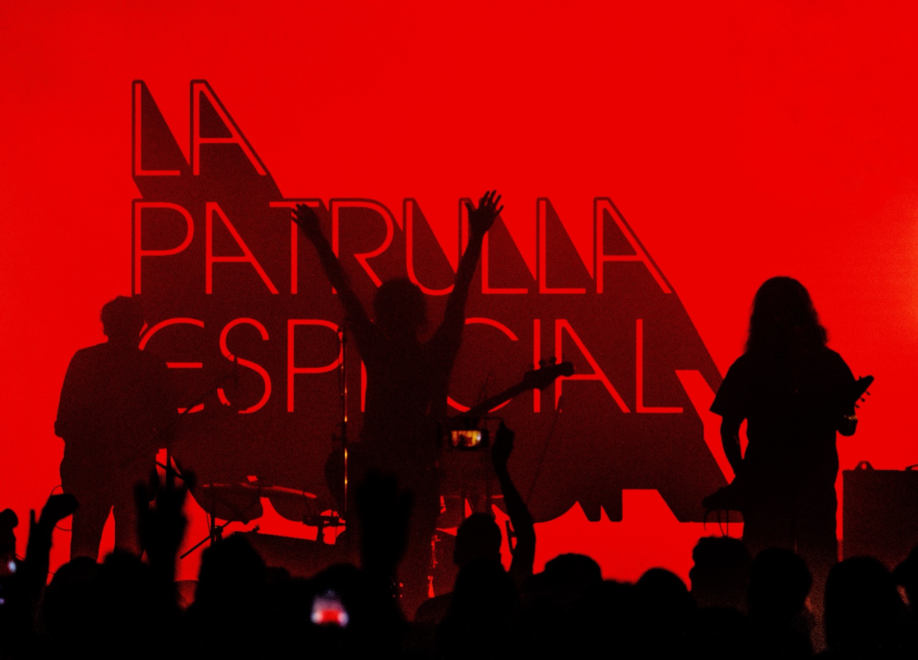 La Patrulla Espacial en vivo frente a su logo, con el público de espaldas y las manos en alto